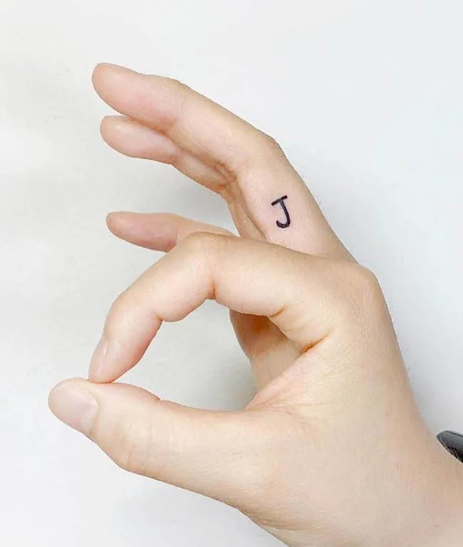 A minimalist initial tattoo on the inner finger