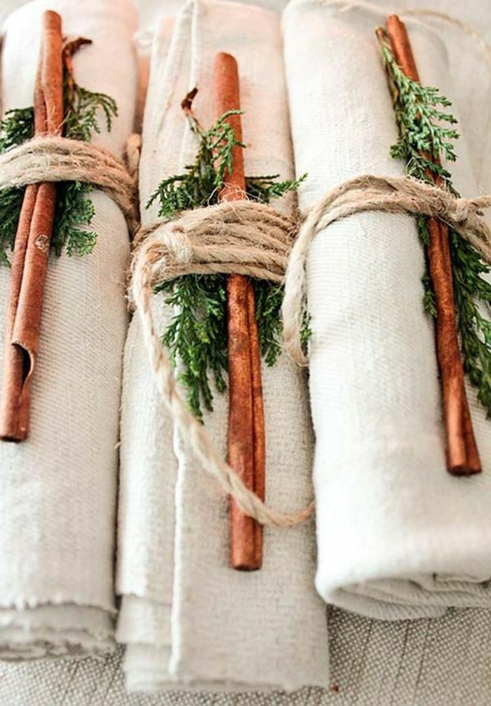 Simple napkin folding with green leaves and cinnamon sticks.