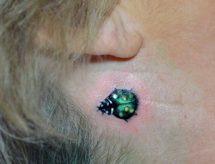 Bold and Brightly Colored Beetle Tiny Tattoo Behind the Ear